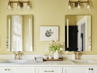 Dual sinks and matching smart mirrors complete the guest bathroom vanity and make room for everyone to start their day feeling fresh and pampered. Soothing neutral walls add warmth to the space while matching brass vanity lights enhance the turn of the century style found throughout the room.